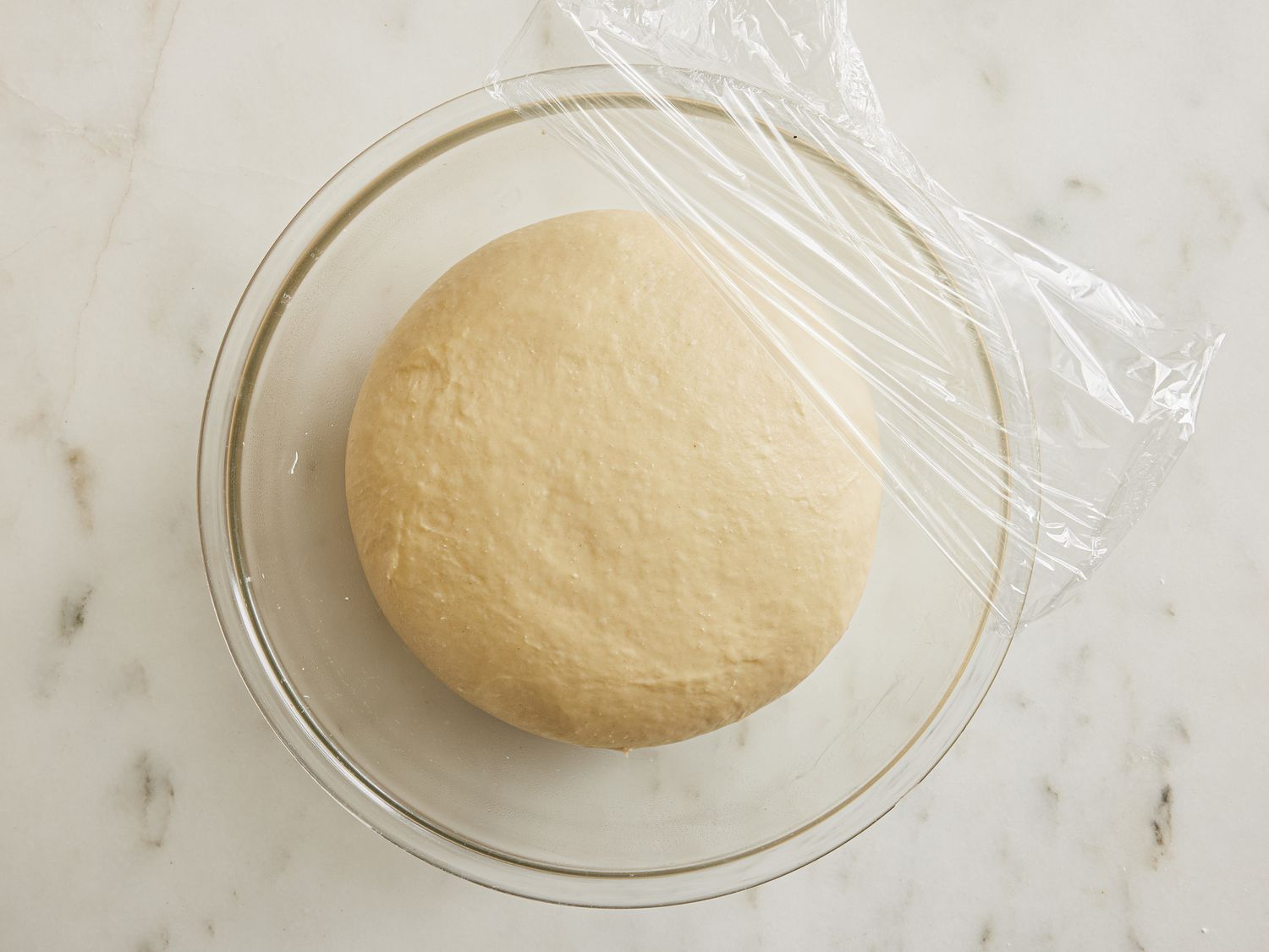 Dough in a glass bowl, after proofing, half covered with plastic wrap