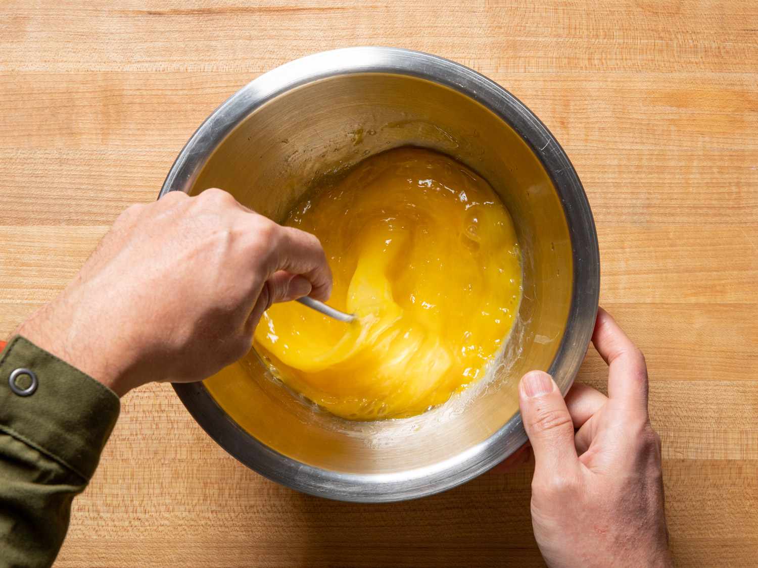 Eggs being scrambled with a whisk in a metallic bowl.