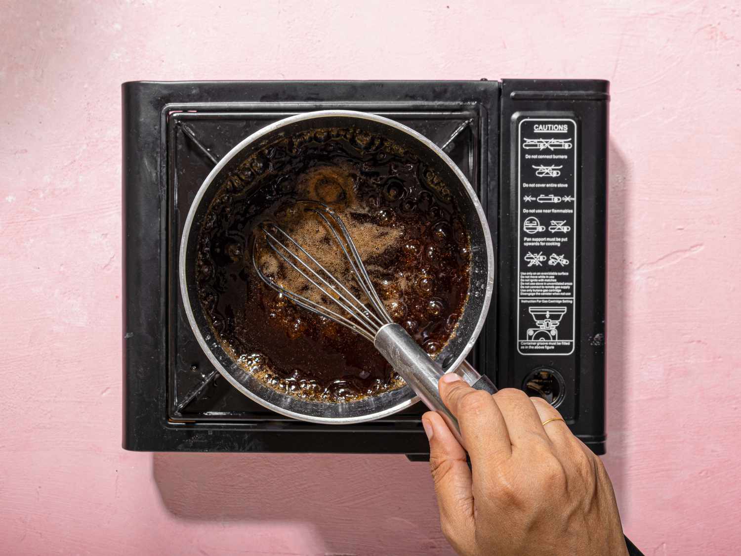 Hand whisking mixture in a saucepan on a portable burner
