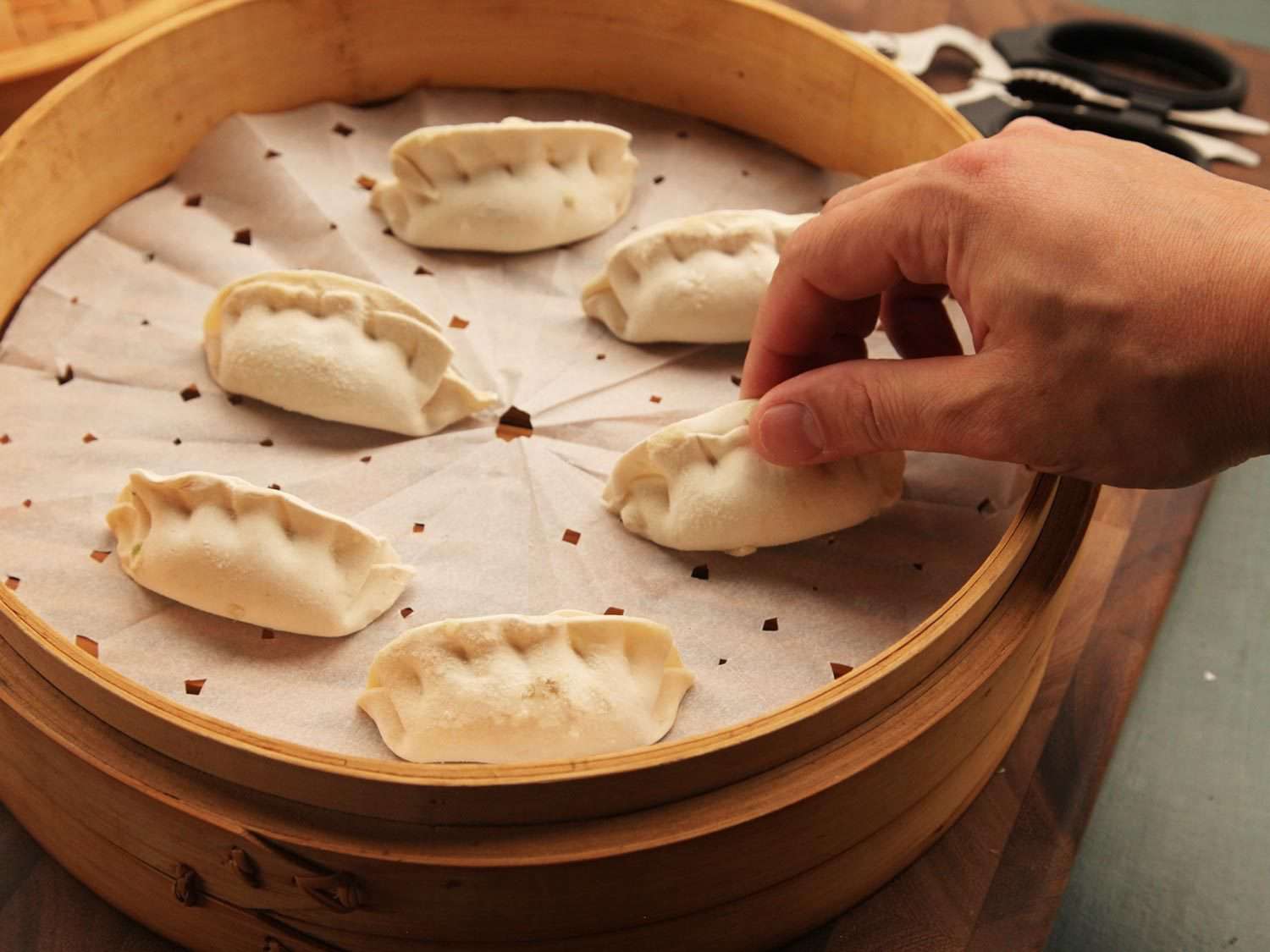 Placing frozen dumplings in steamer basket.