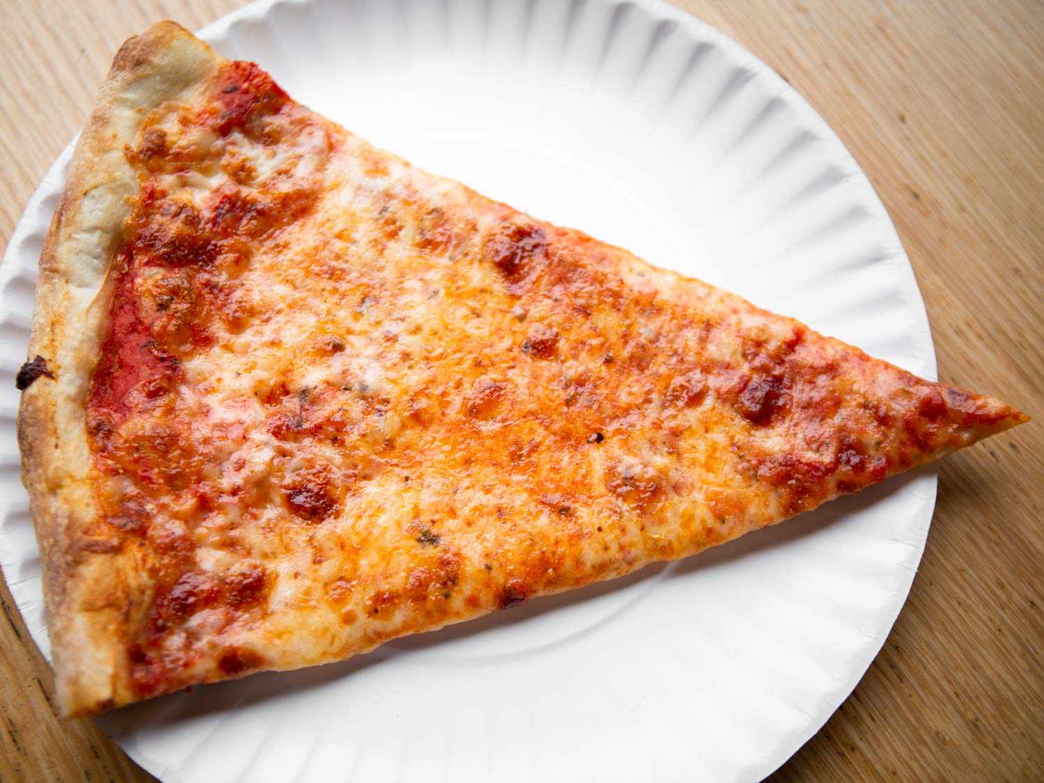 A slice of New York style cheese pizza on a white paper plate. 