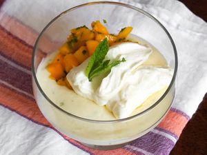 A Lime Posset With Mint and Mango Fruit Salad in a glass dish with mint leaves and whipped cream on top. 