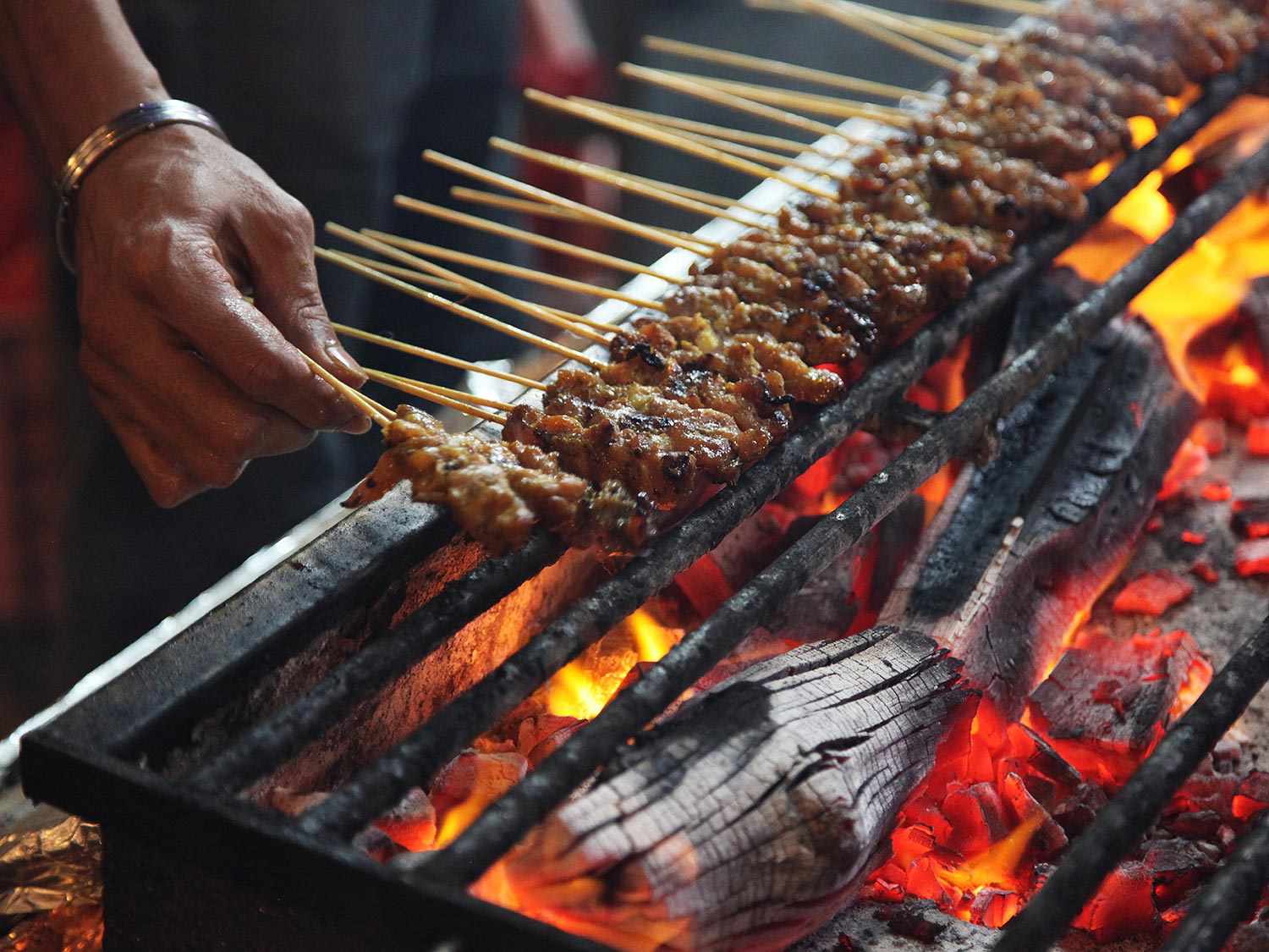 Small skewers of satay being cooked over a grate in Singapore.
