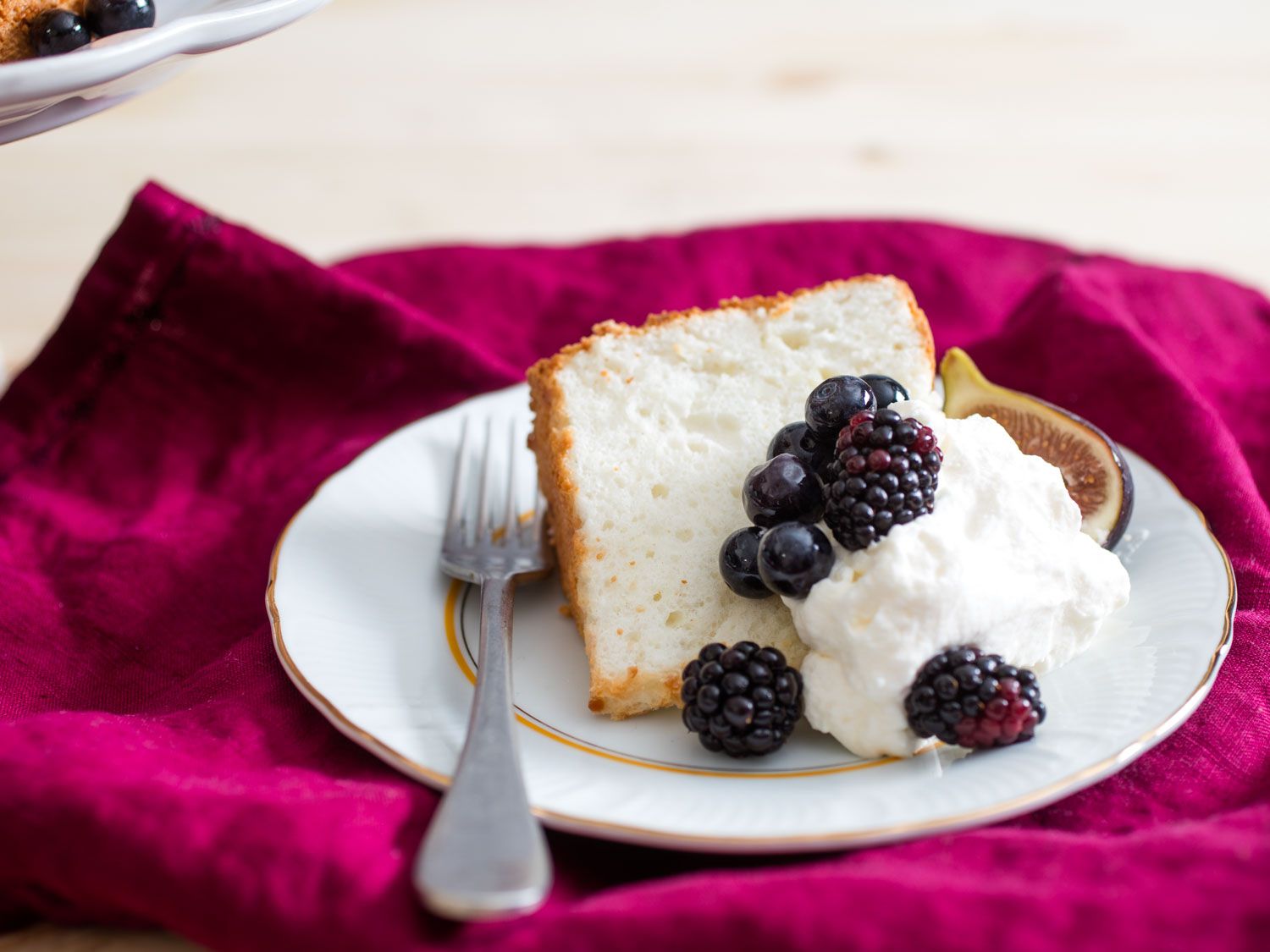 A slice of angel food cake on a dessert plate, garnished with whipped cream and blackberries.