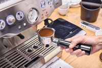 A person places a portafilter filled with coffee grounds into the Breville The Barista Express Espresso Machine