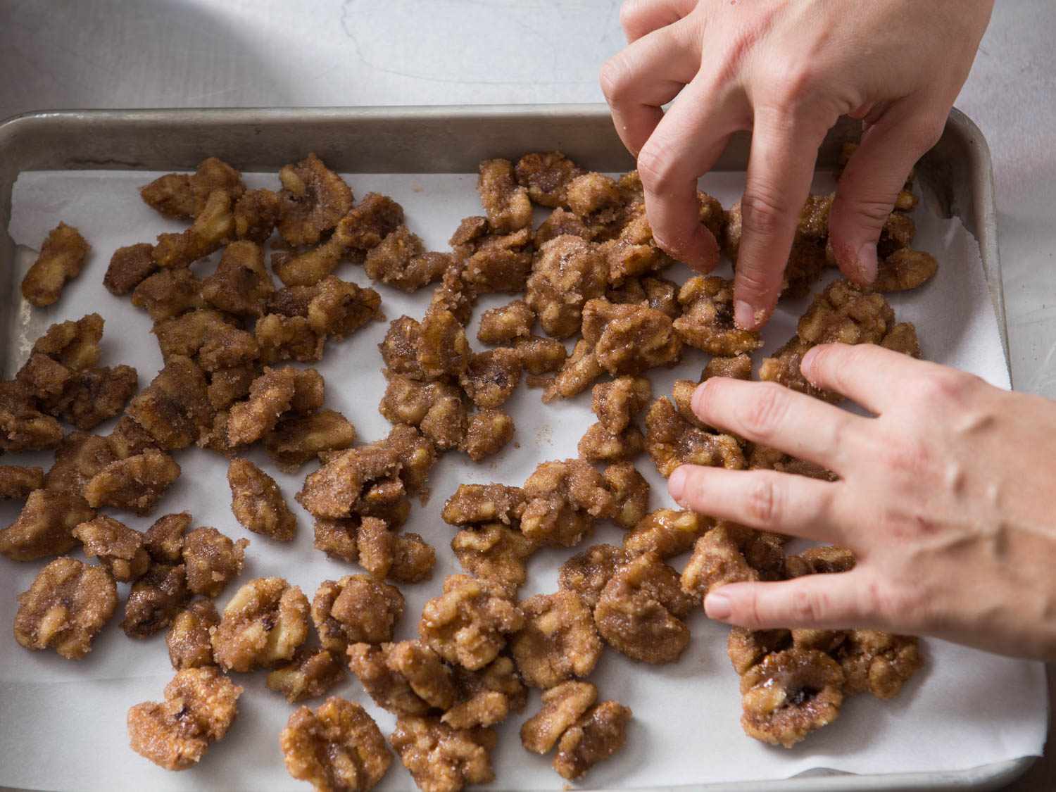 Arranging sugar- and spice-coated walnuts on a parchment-lined baking sheet before roasting.