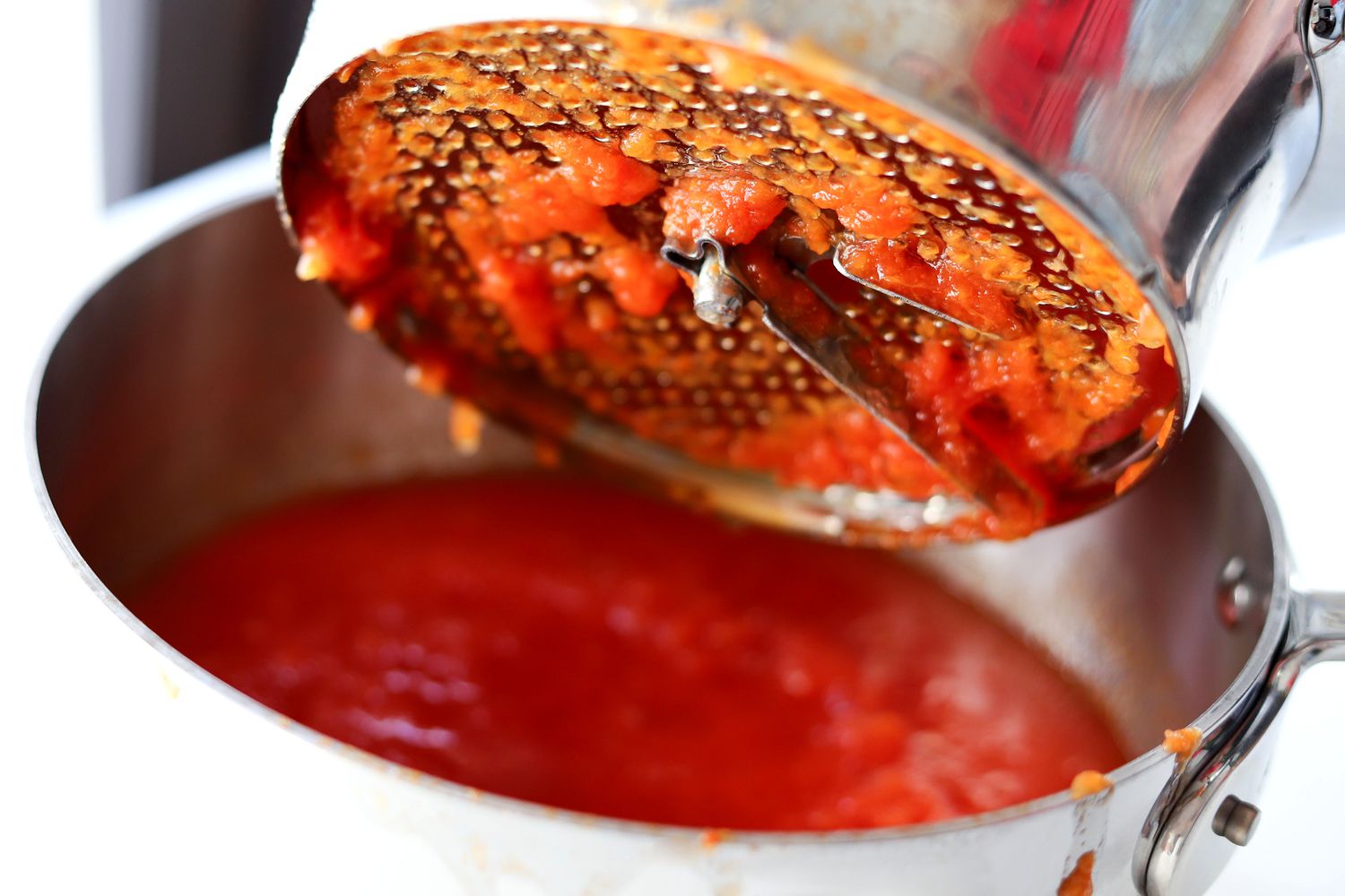The underside of a food mill with tomatoes being strained through it into a pot