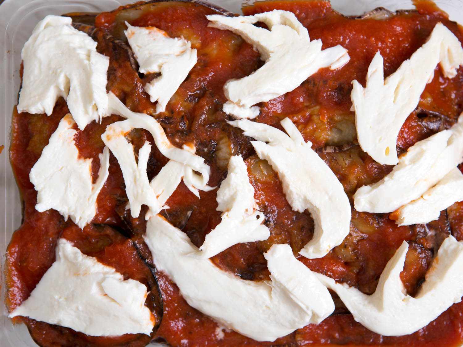 Overhead view of torn shreds of fresh mozzarella on top of Eggplant Parm