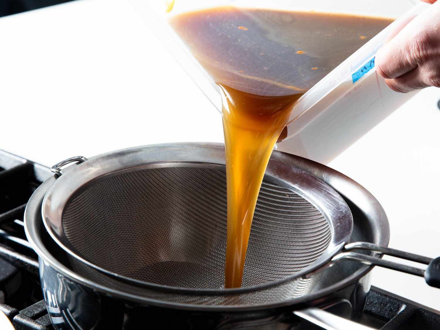 Chilled brown duck stock is strained into a saucepan.