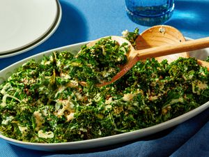 A dish of roasted kale salad with wooden serving spoons on a blue tablecloth
