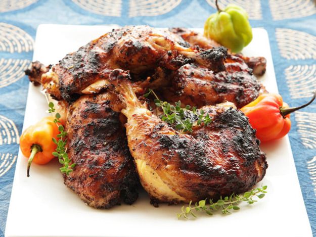 A white square platter of grilled jerk chicken with brightly-colored Scotch bonnet peppers.