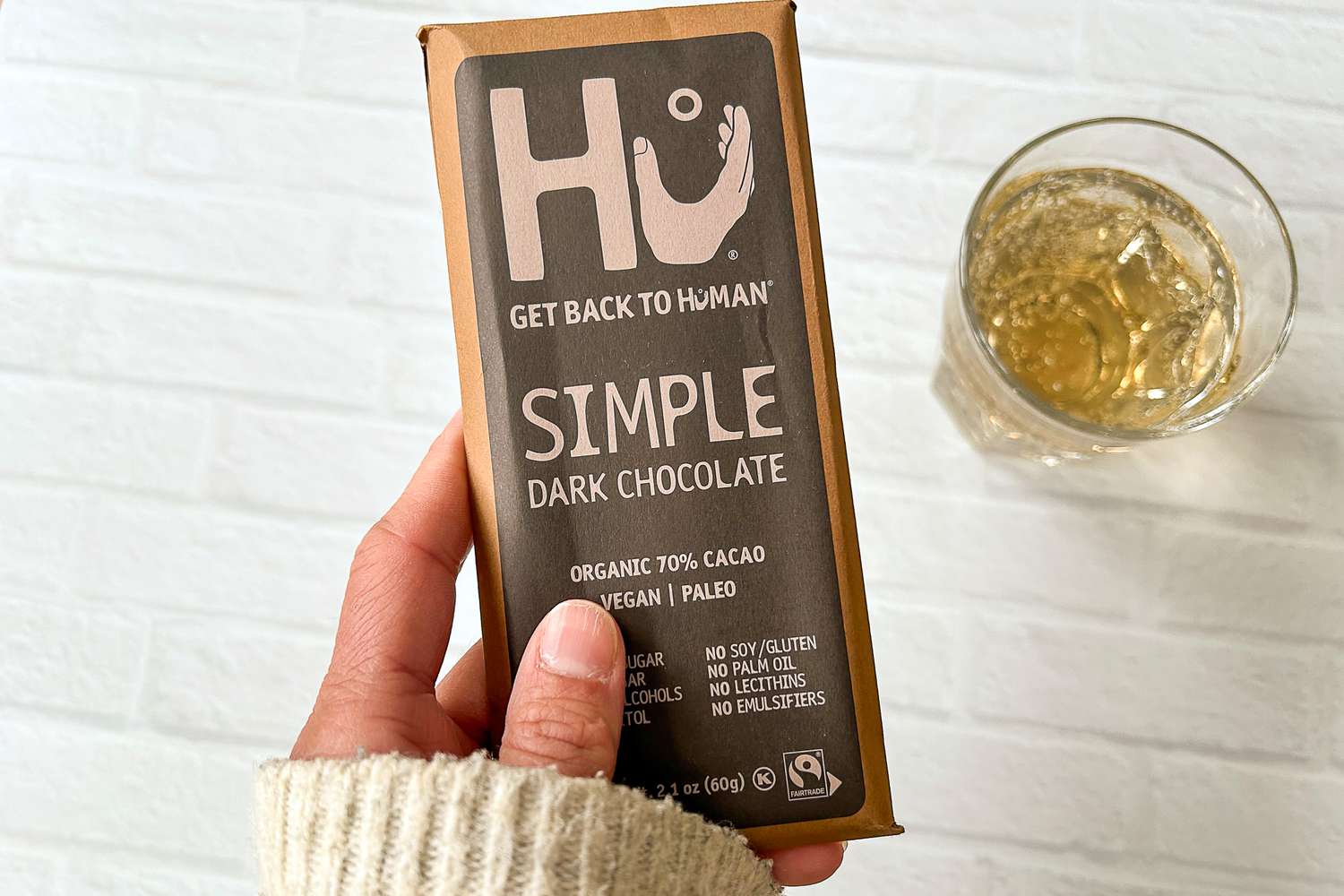 A hand holding Hu Simple Dark Chocolate next to a glass
