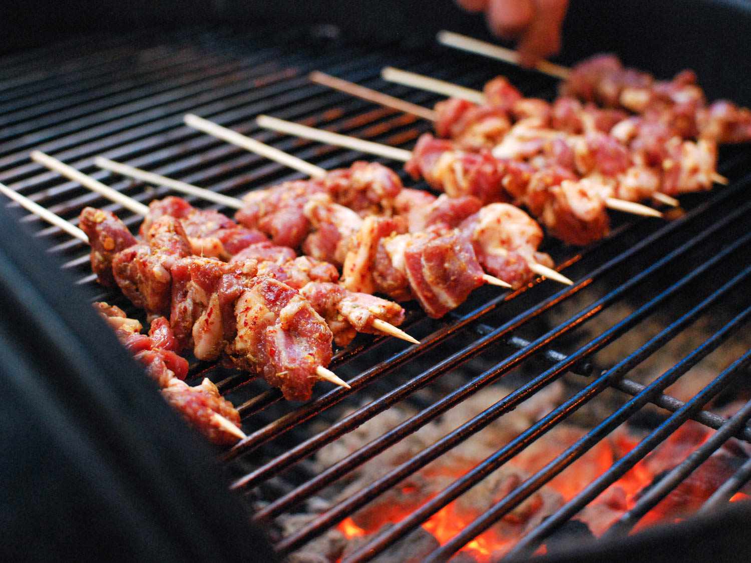 Nine lamb skewers cooking over indirect heat on a charcoal grill.