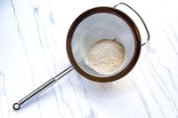 Rösle Stainless Steel Round Handle Kitchen Strainer with a portion of sifted flour on a marble surface