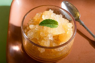 A glass bowl of granita topped with a single mint leaf, placed next to a spoon