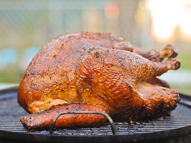 The fully cooked, golden brown smoked turkey on the surface of a charcoal grill.