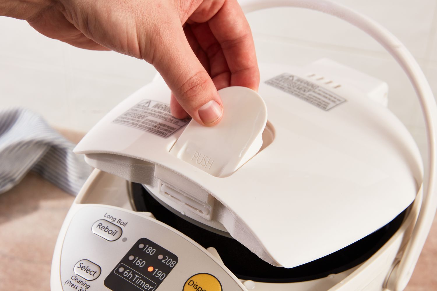 A person lifting up the lid of the Panasonic hot water dispenser.