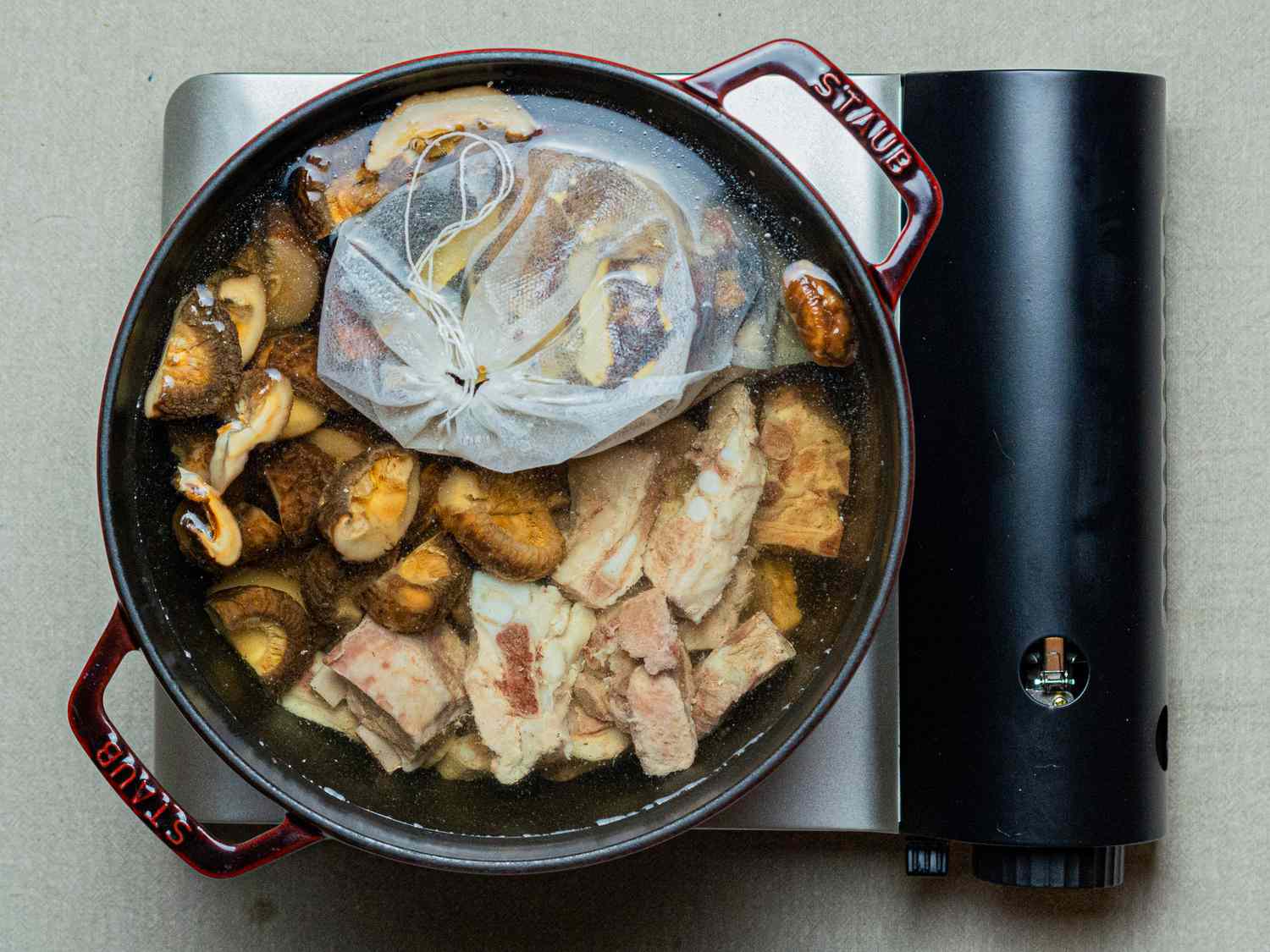 Overhead view of mushrooms, spice bag and bones cooking in pot
