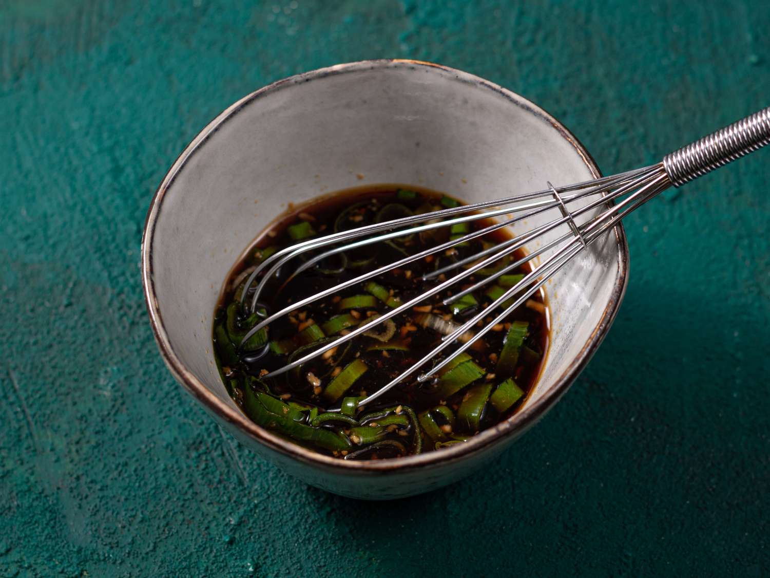 Sauce ingredients in a small ceramic bowl with a metal whisk inserted.