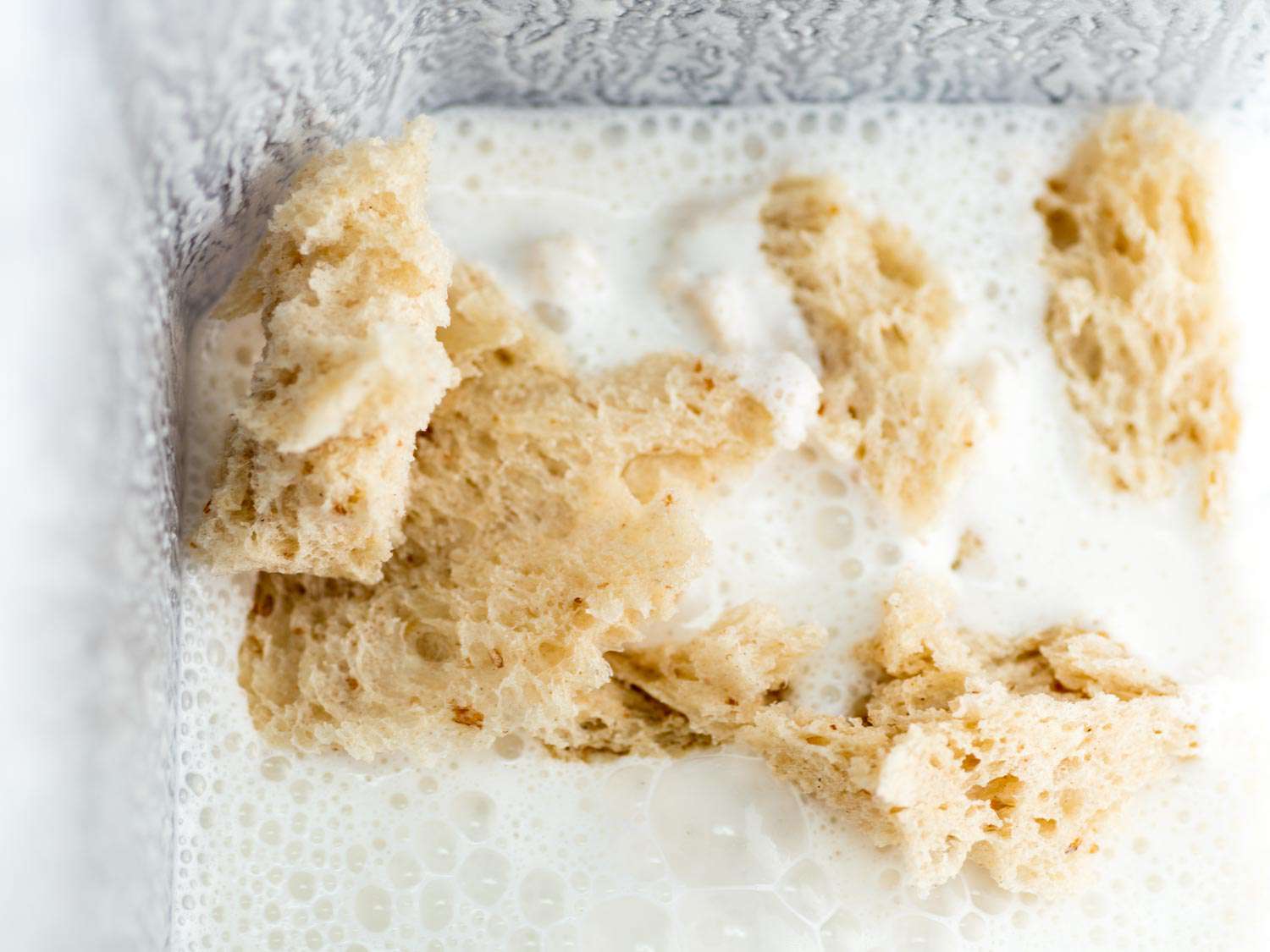 Pieces of torn bread in a blender containing blended almond and water for ajo blanco base. 