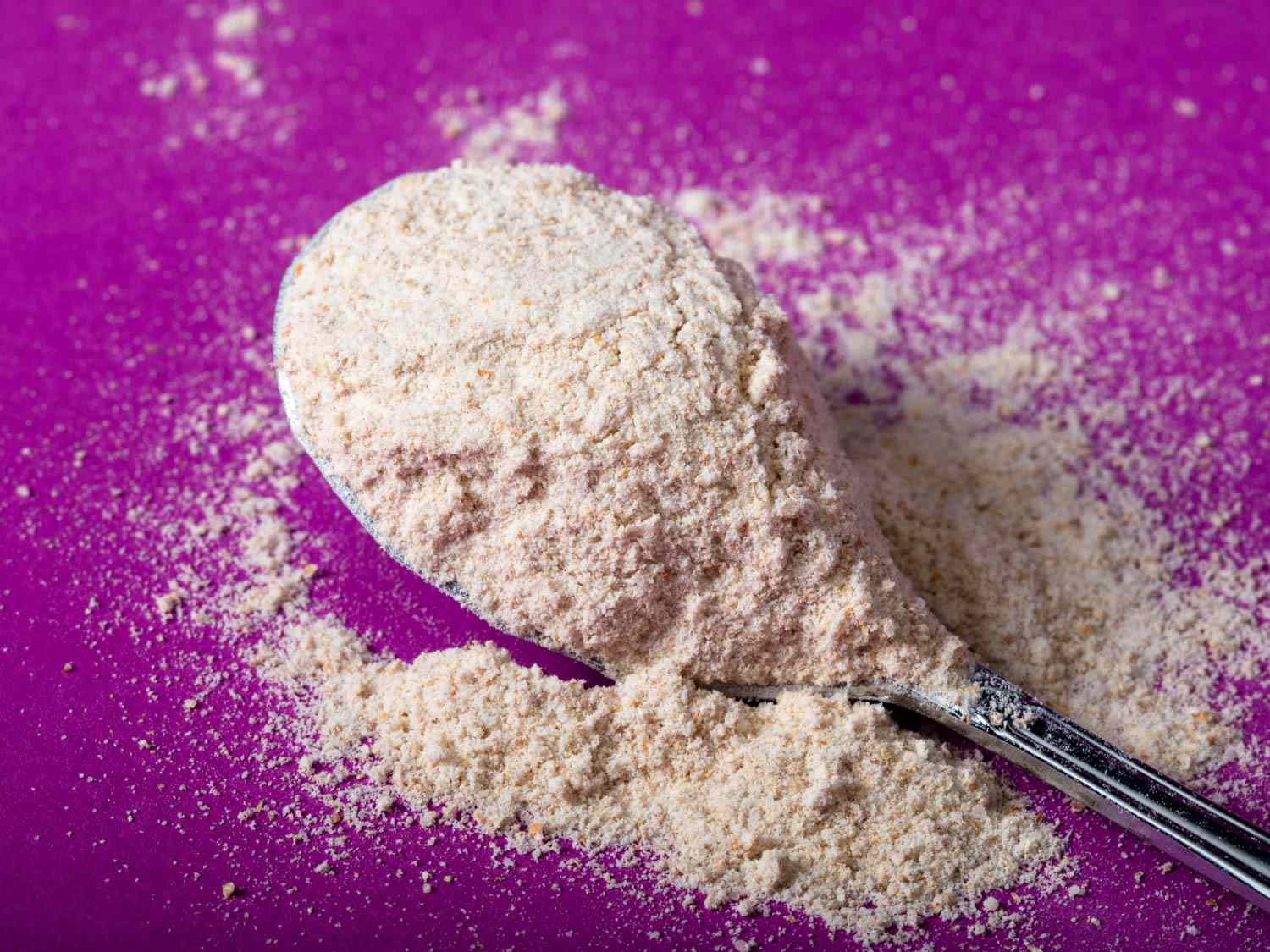A spoonful of flour on a orchid color surface.