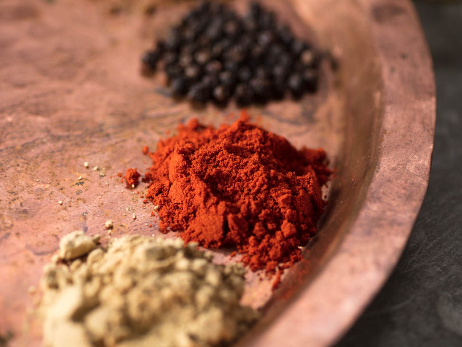A copper tray with spices on it. Kashmiri chile powder is in the center of the image.