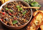 Overhead view of caponata, served in a wide bowl with toasted slices of ciabatta.