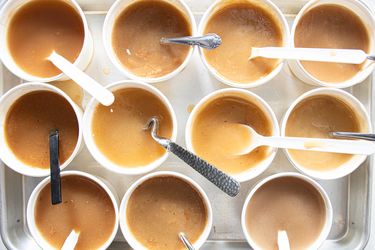 A tray of cups filled with gravy samples each containing a spoon or utensil for tasting