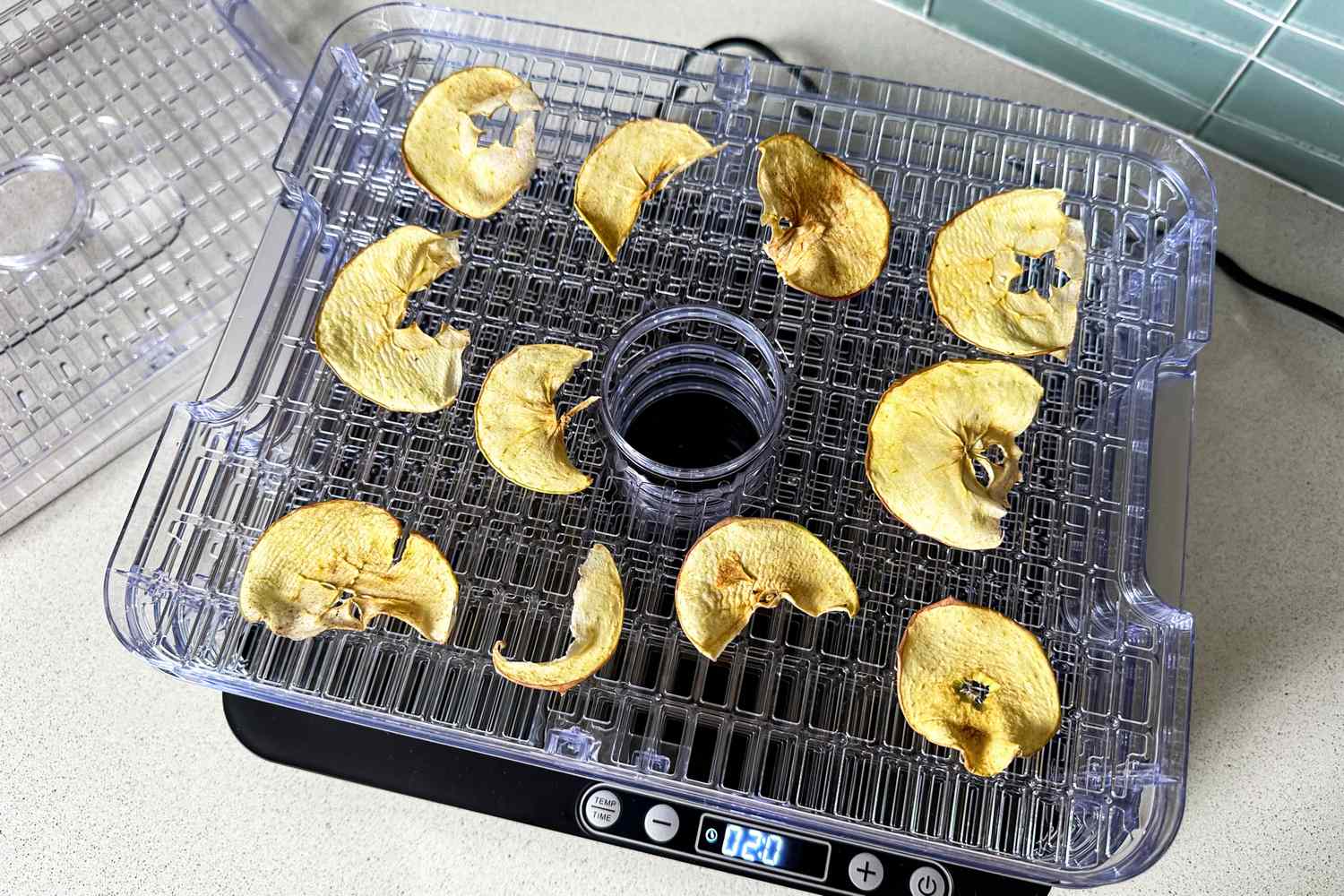 Slices of dried apple arranged on a Nesco Digital 5 Rectangular Dehydrator with a transparent lid and digital timer display