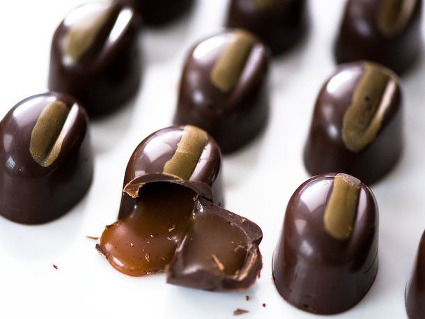 A tray of beautiful chocolate bonbons, with one cracked open to reveal a runny caramel filling.