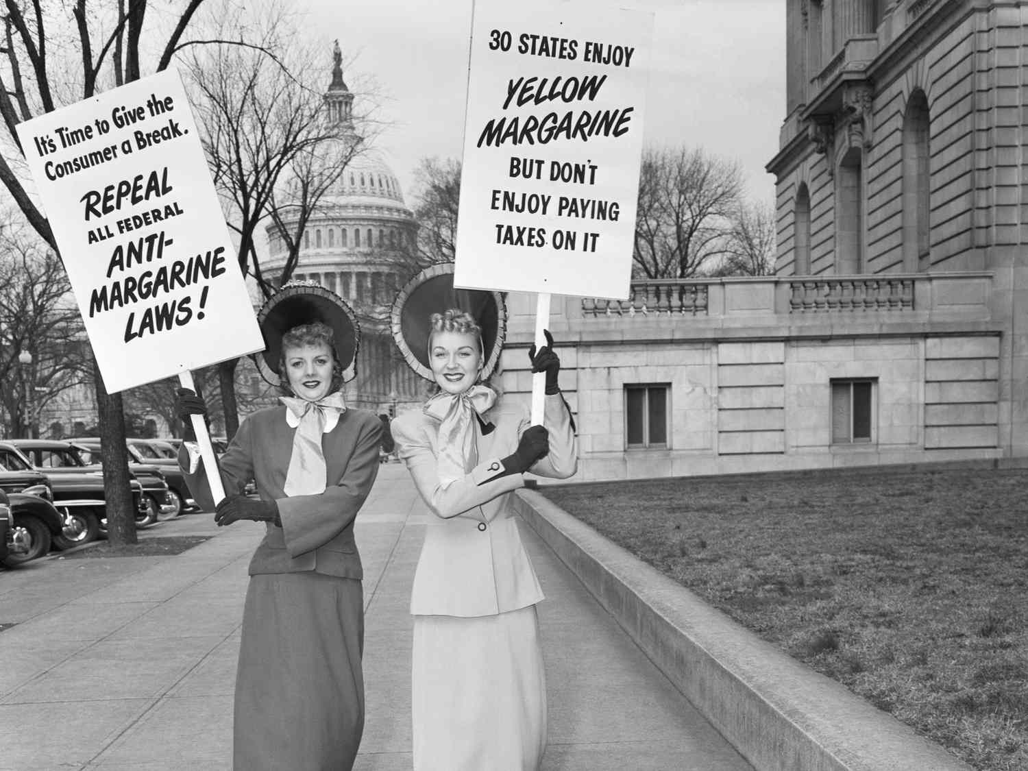 Two women in vintage clothing holding protest signs related to antimargarine laws in front of the US Capitol building