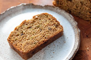 A slice of freshly baked zucchini bread, served on a ceramic plate with an irregular rim.