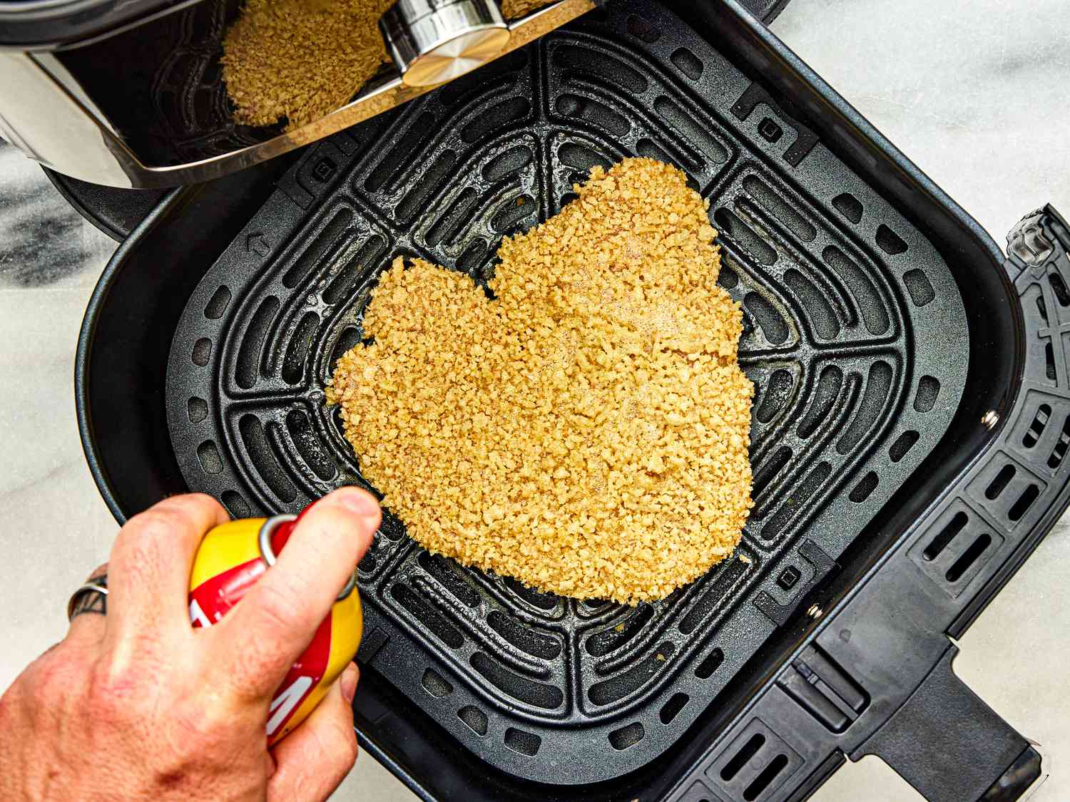 The panko-coated cutlet is spritzed with cooking spray in the air fryer basket.