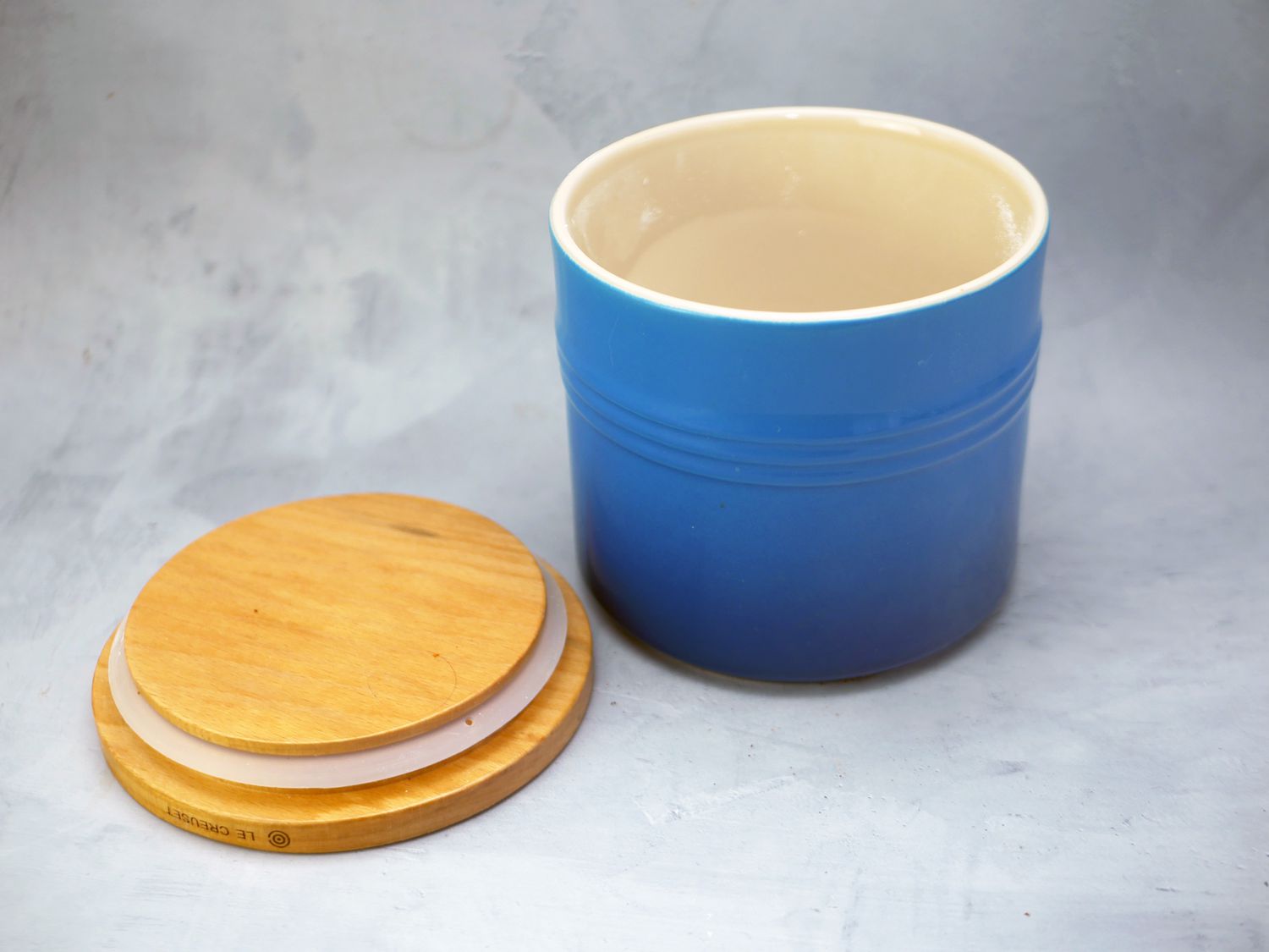 Le Creuset container with wooden lid off to the side on a gray surface