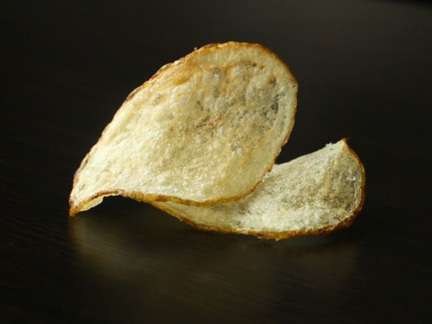 Closeup of two extra crispy potato chips set on a black surface.