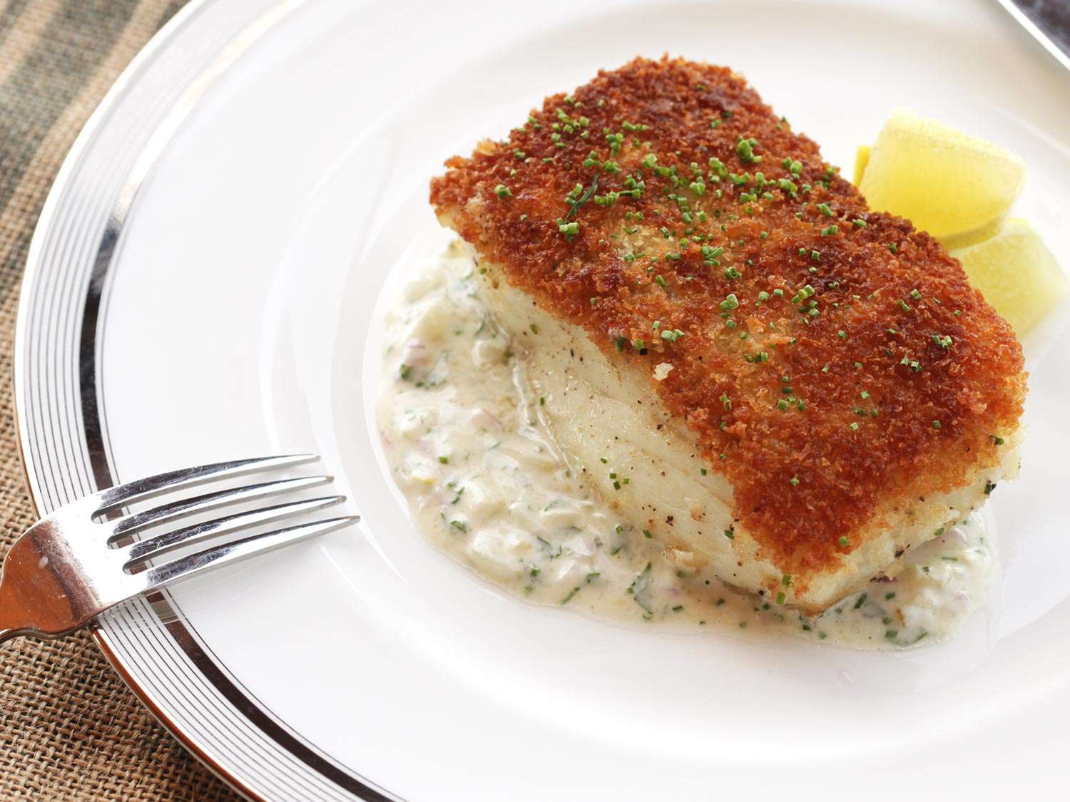 A piece of pan-seared fish with a crispy crumb coating on top, sprinkled with chopped herbs. 