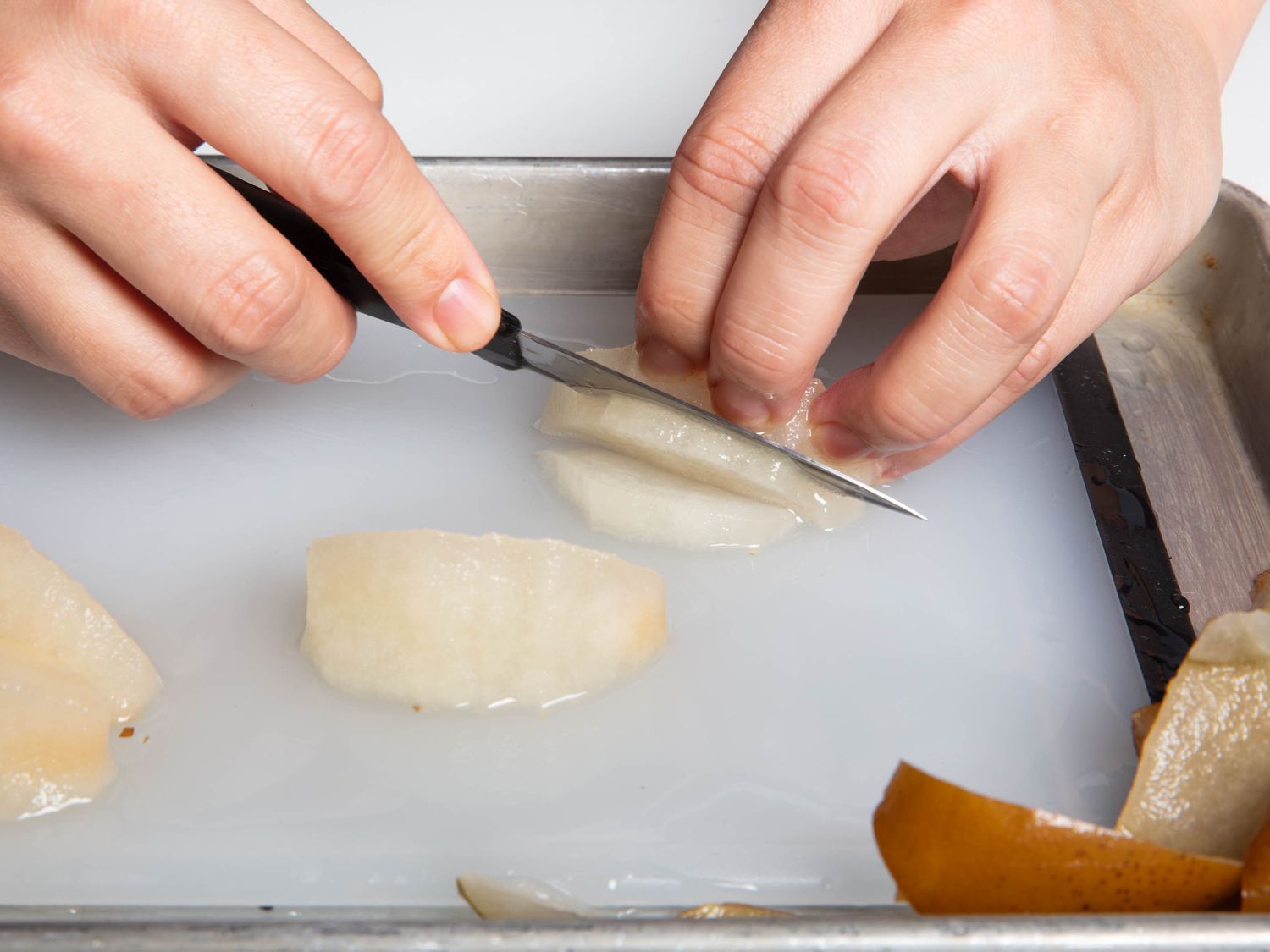 Thawed frozen pear being sliced on a cutting board set in a rimmed baking sheet