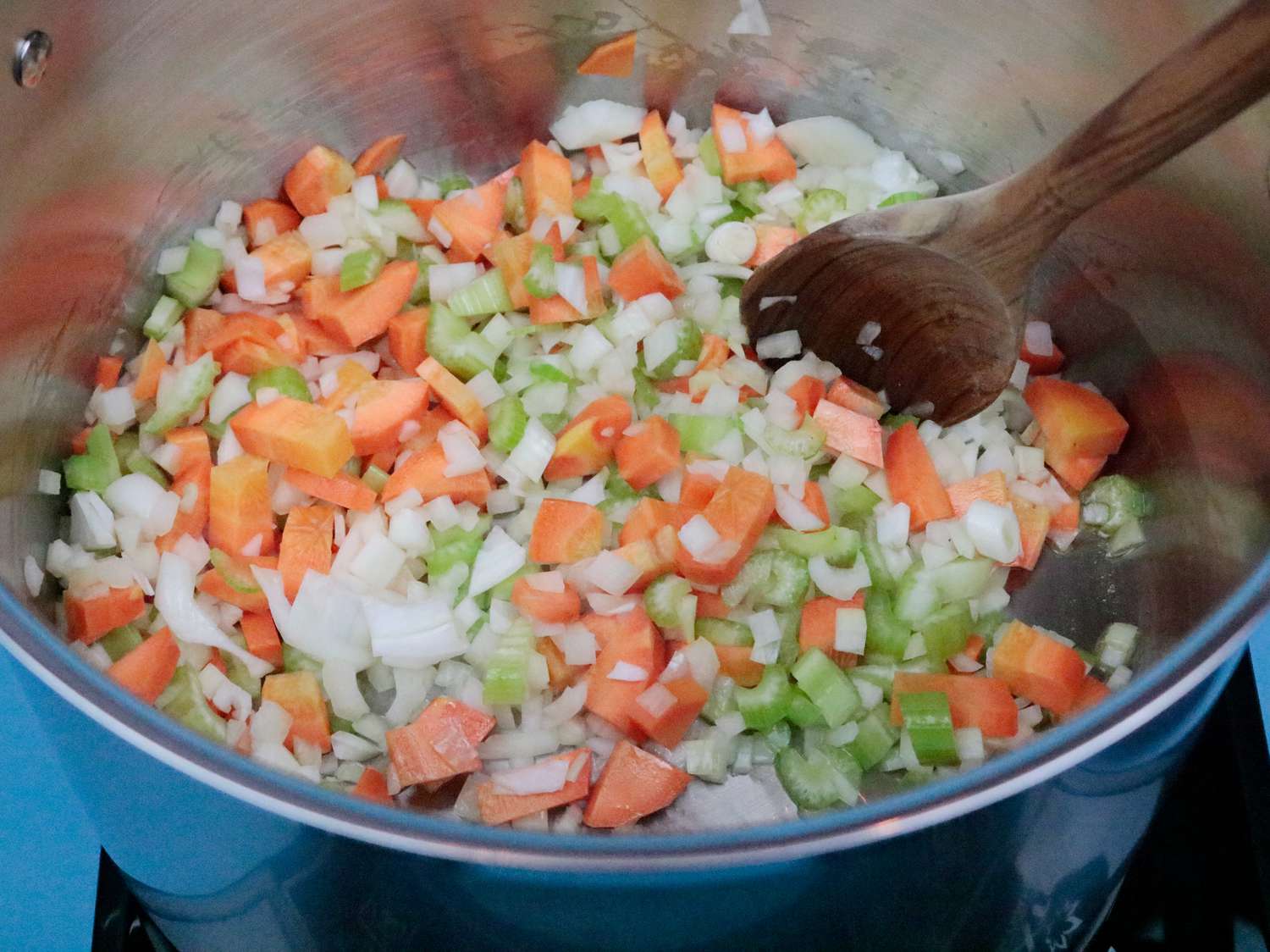 A stainless steel stockpot cooking a mixture of chopped onions, carrots, and celery.