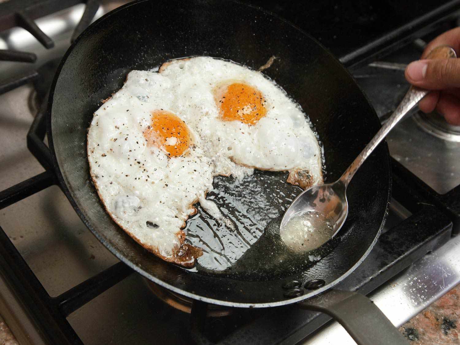 Basting oil on egg whites in a tilted pan. 