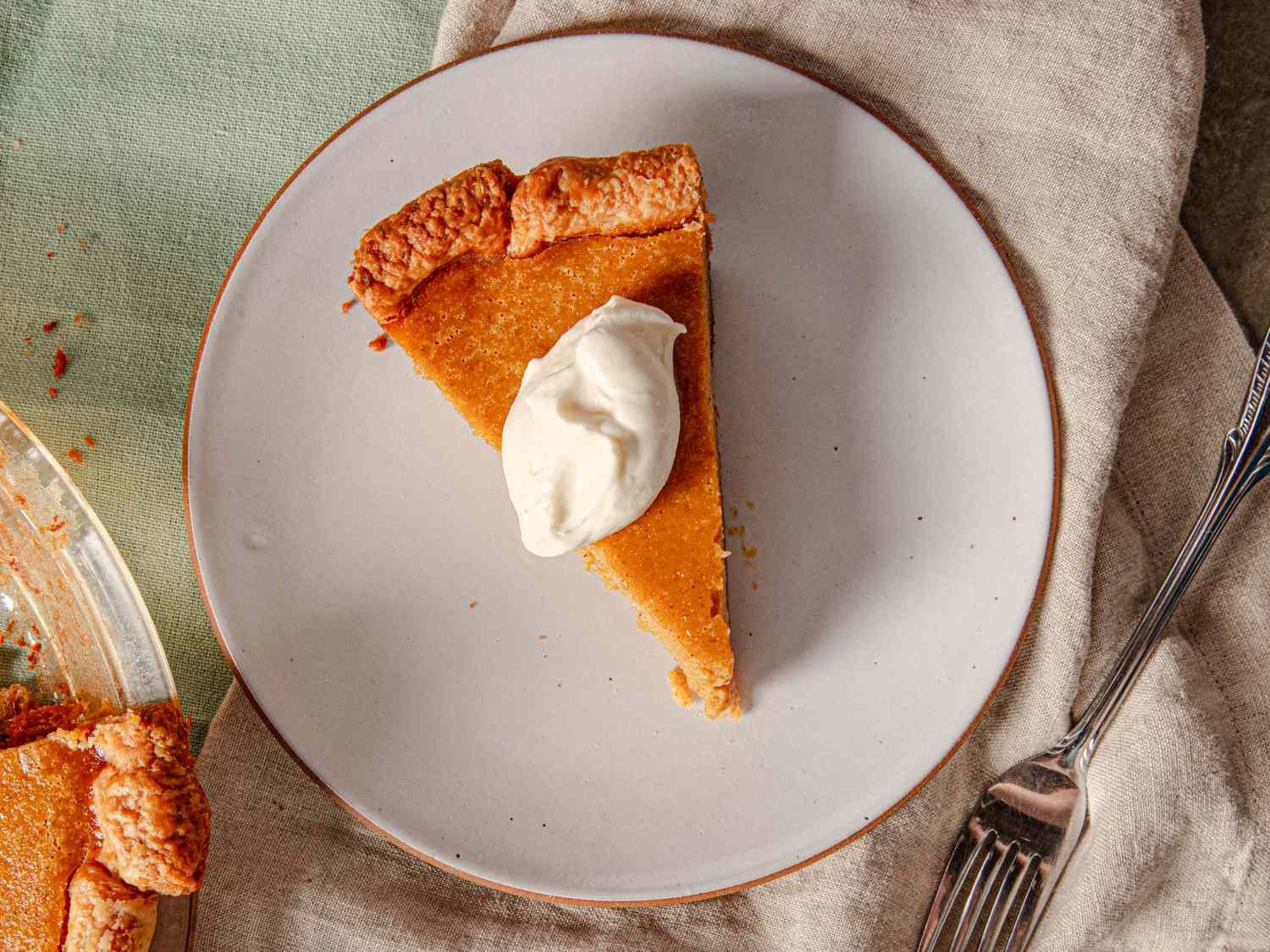 A slice of pumpkin pie topped with a dollop of whipped cream on a plate with a fork placed beside it on a table