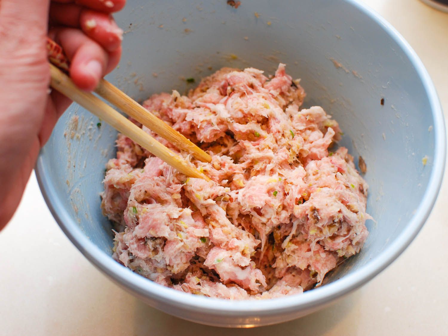 Additional ingredients are mixed into the sheng jian bao filling in a small bowl with a pair of chopsticks.