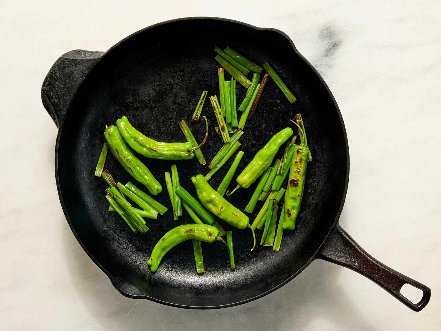 A black skillet containing cooked green peppers and vegetables