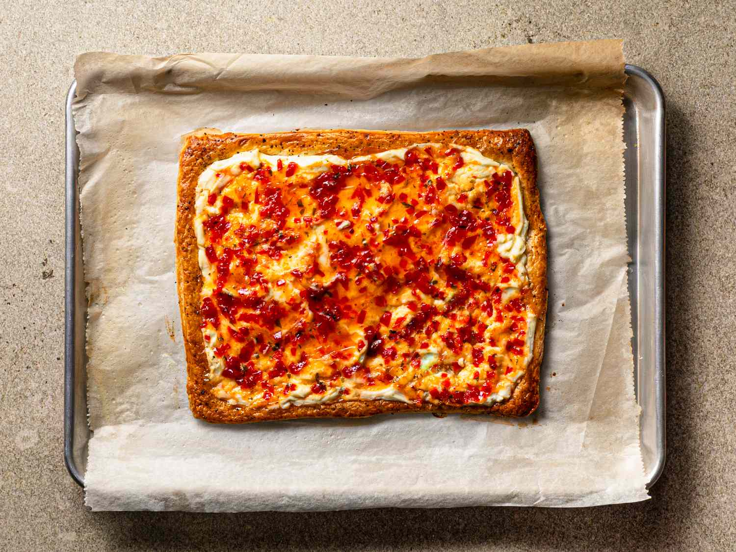 A cheese and pepper jelly tart on parchment paper on a baking tray