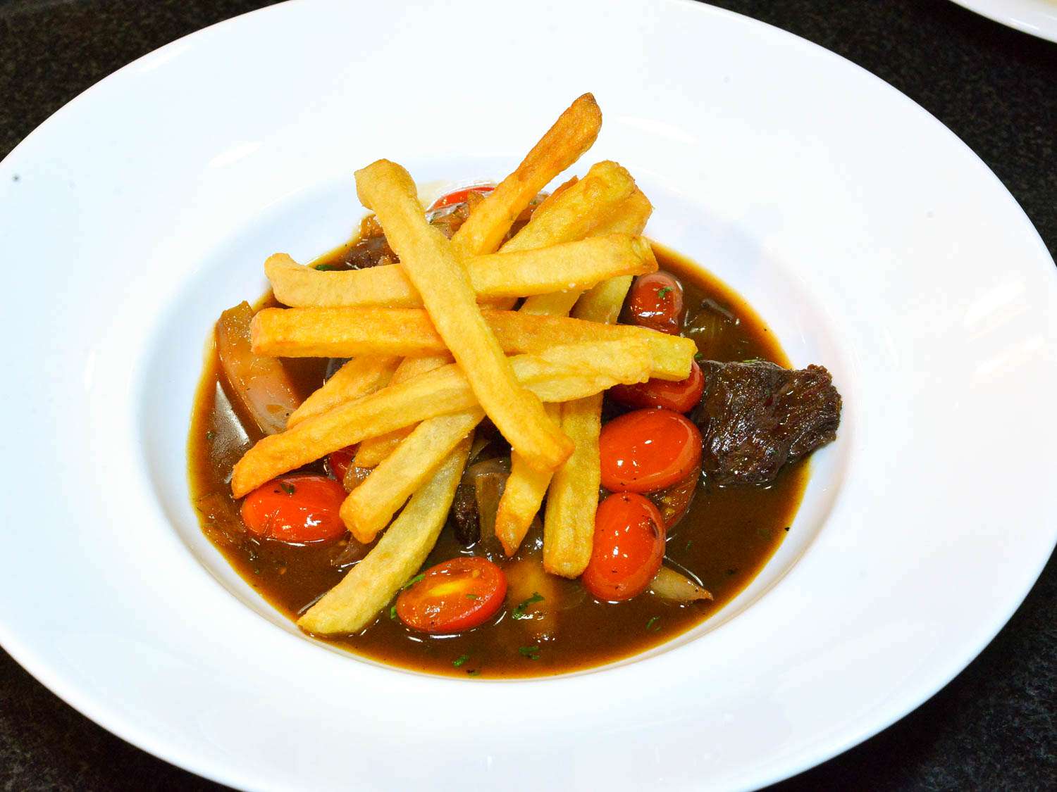 A platter of Peruvian lomo saltado (stir-fried beef) topped with french fries.