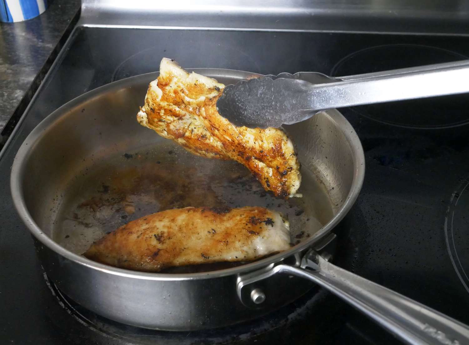 a person flipping chicken in a saute pan