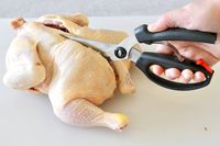 A person using poultry shears to snip out a chicken's backbone.
