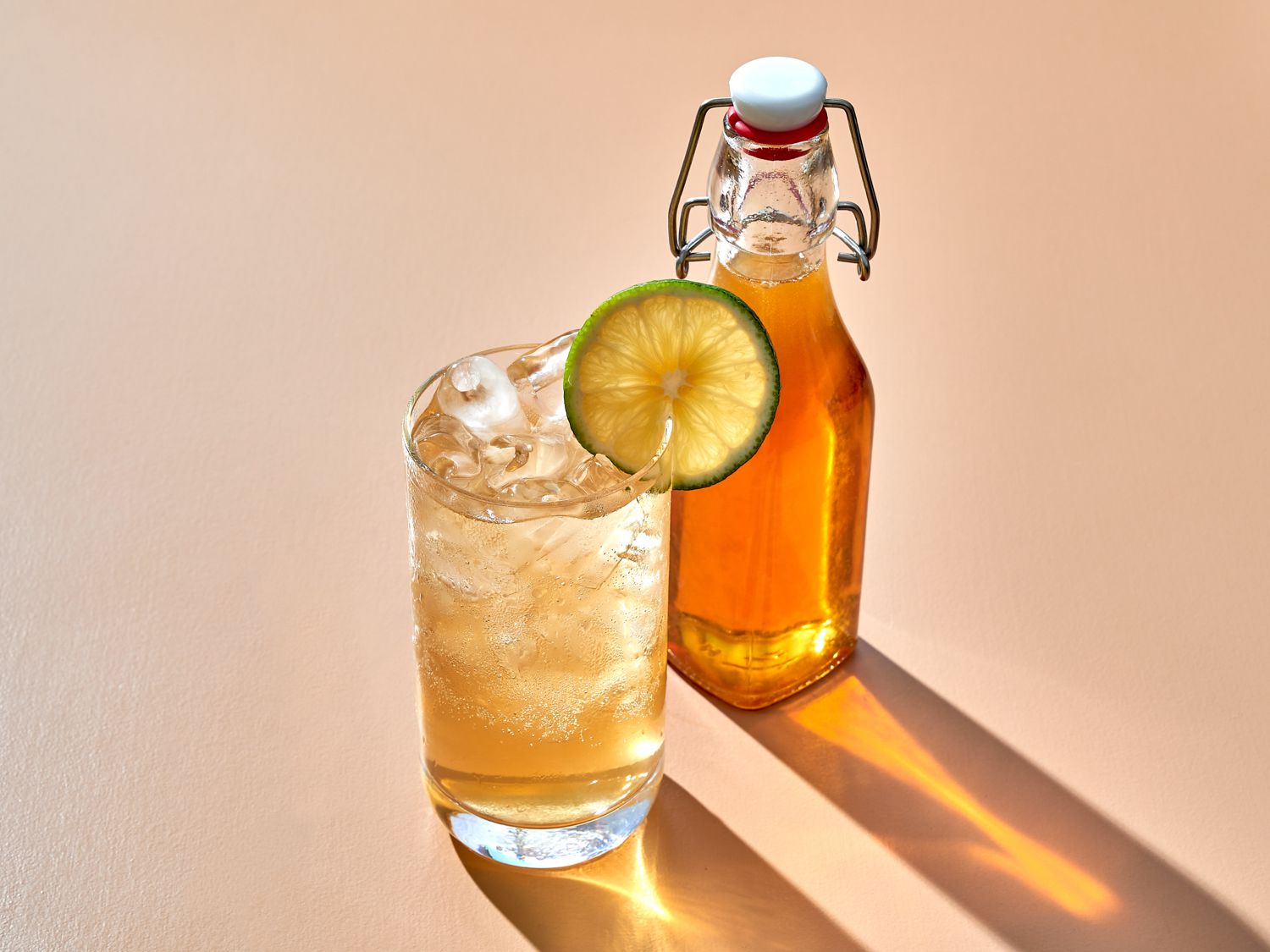 Tonic syrup combined with sparkling water in a glass with ice, bottle of tonic syrup in the backround