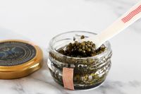 An open jar of Caviar Co osetra caviar with a mother-of-pearl spoon inside