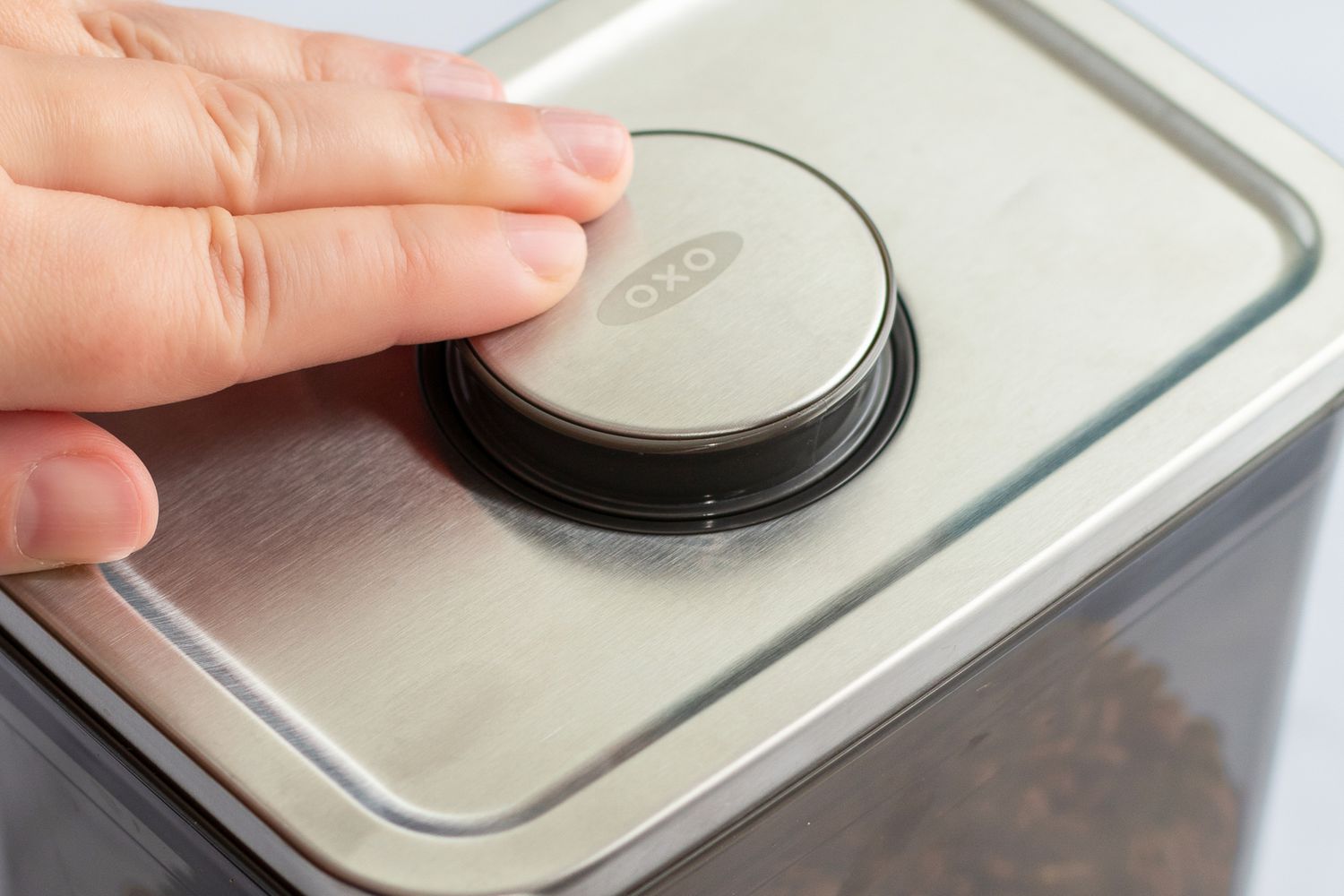 A hand pushing the top of the The OXO POP Coffee Container