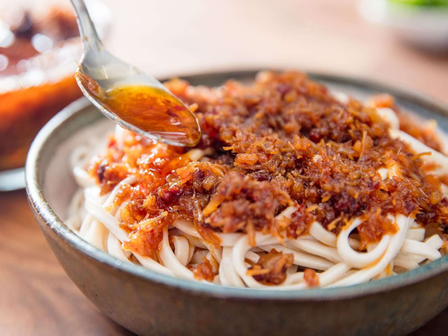 Spooning XO sauce over a bowl of noodles.